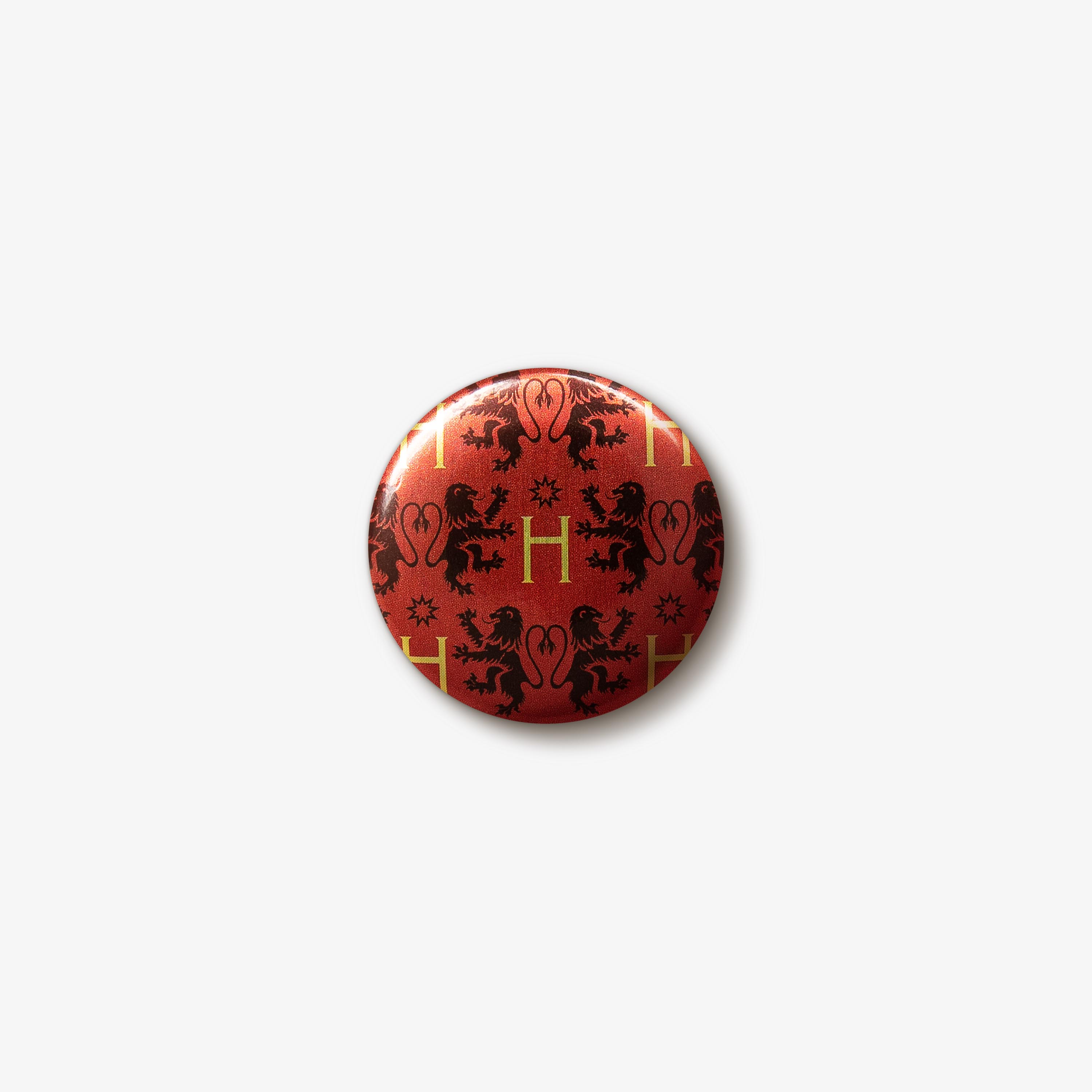 Red button badge with a repeating pattern of black Gryffindor lion emblems and gold ‘H’ letters.
