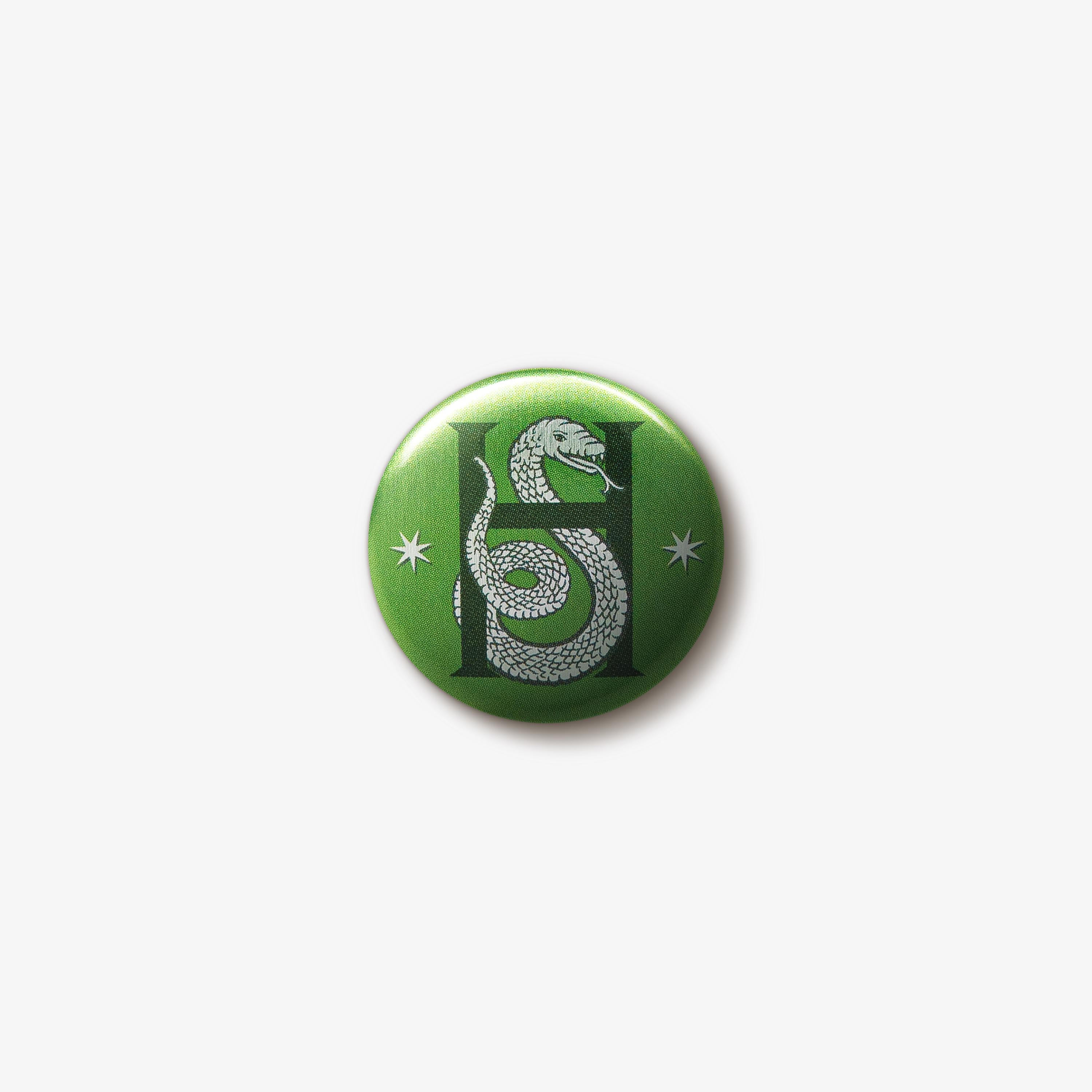 Green button badge featuring a silver Slytherin snake emblem intertwined with a dark ‘H’ letter in the centre. There are two silver seven-pointed stars either side of the emblem.